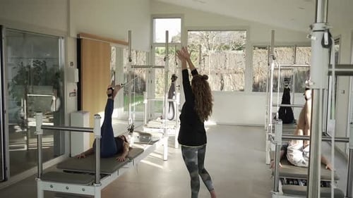 People doing exercises on pilates reformer with help of instructor