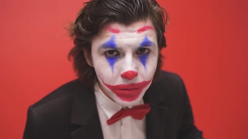 A Clown with Colorful Makeup Poses on an Isolated Red Background a Joyful Magician or a Mysterious