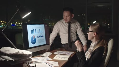 Man and Woman Discussing Charts at Night in Office