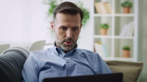 Man Talking To Laptop On Couch At Home