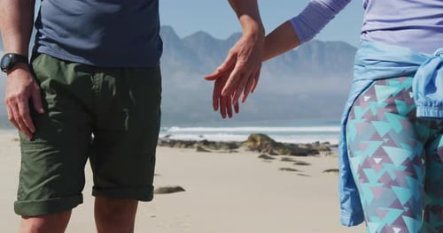 Mid section of senior hiker couple holding hands on the beach.