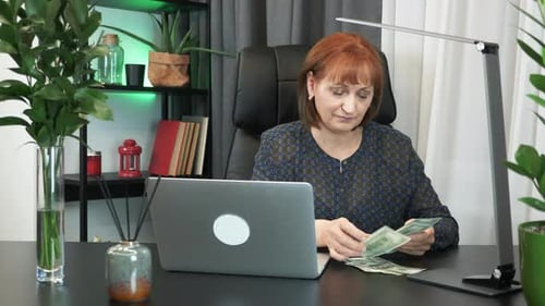Middle-aged businesswoman is counting money sitting in her modern office
