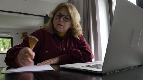 Woman Works at Laptop, Writing on Paper at Home