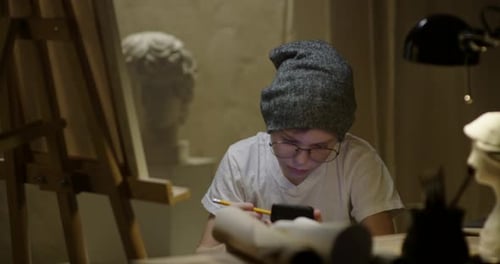 Boy with Glasses and Cap Uses Phone in Studio