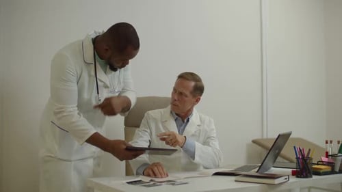 African American Doctor and Experienced Male Colleague Discussing Medical Test Report on Tablet Pc