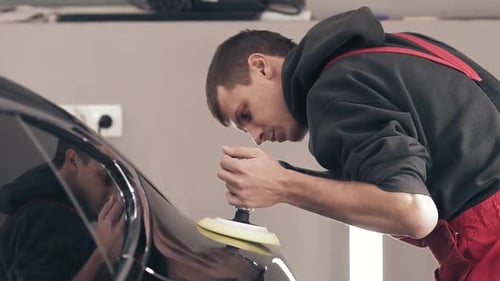 Man Polishing Black Car Hood in Auto Garage