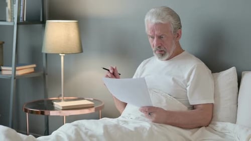 Adult Man Reads Document in Bed