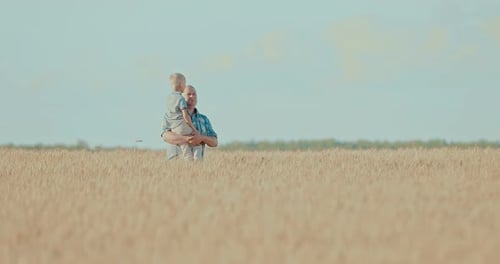 Dad Holds His Son in His Arms and Walk Across the Field