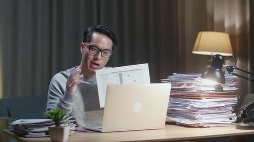 Man Explains Spreadsheet via Laptop Video Call at Desk