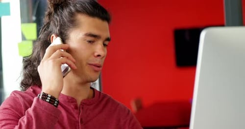 Young Adult Talking on Cellphone at Office Computer