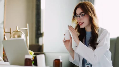 Woman Doctor Holding Medicine Bottle During Online Consultation