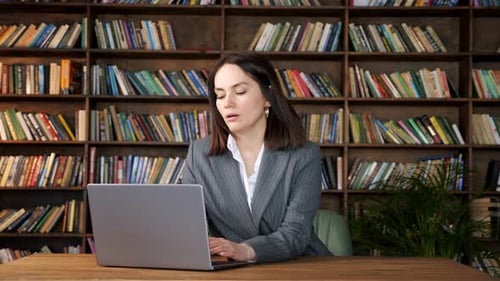 Woman Uses Laptop At Desk In Front of Bookshelf