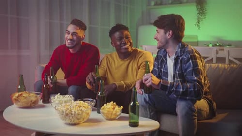 Three Multiethnic Guys Enjoying Friday Evening Together Watching Tv and Cheering with Beer at Home