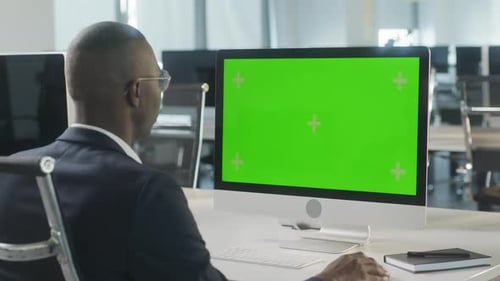 Business AfricanAmerican Man Working on Desktop Computer with Green Screen Mock Up Display in Busy