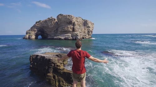 Young Man Reaches Out at Ocean Rocky Coast