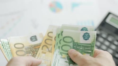 A Businessman Hands are Counting Euro Bill Notes on Background of Calculator and Graphs
