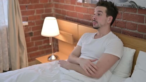 Jeune homme bouleversé assis et inquiet au lit