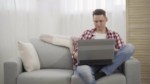 Young Adult Using Laptop on Sofa at Home