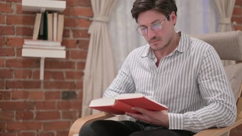 Man Reads Book Sitting in Chair at Home