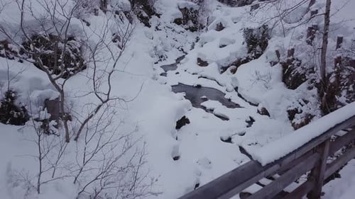 Winter wonderland.Snowy valley with a creek in the alps. Drone flying backwards in a gorge above a b