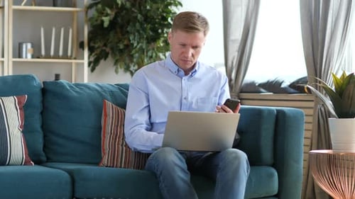 Adult Using Laptop and Phone While on Sofa