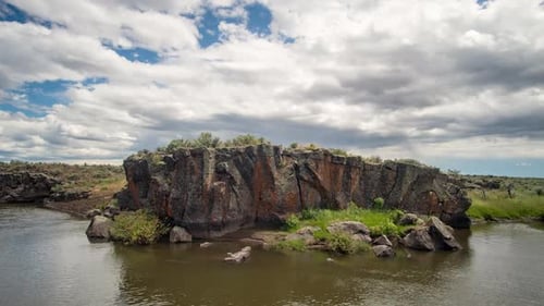 Zeitraffer dicker Wolken, die sich über bunten Felsen entlang des Flusses bewegen