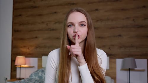 Junge Frau bittet darum, still zu sein, mit dem Finger auf den Lippen, die geheime Stille nicht zu erzählen, indem sie ihren Mund reißt