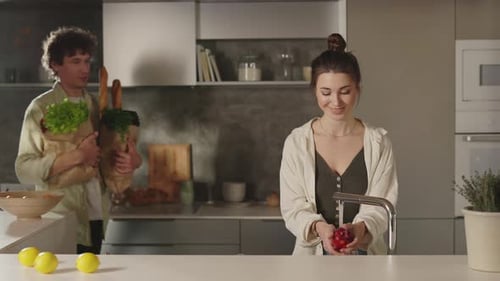 Man Bringing Two Grocery Bags to Woman on Kitchen