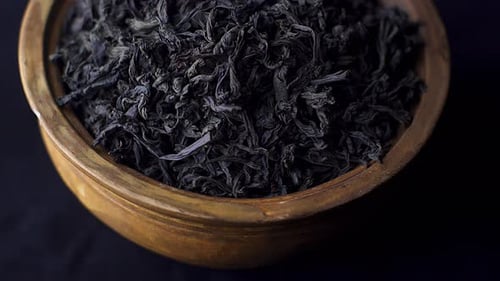 Close up view dry black ceylon tea leaves rotate in a clay bowl on black background