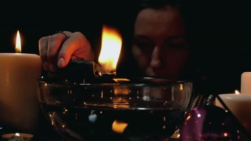 Hand Holds Burning Stick Above Water with Candles