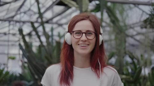Woman Smiling with Headphones in Greenhouse among Cacti