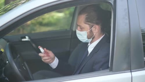 Side View Young Man in Covid19 Face Mask Sitting on Driver's Seat Spraying Disinfectant on Steering
