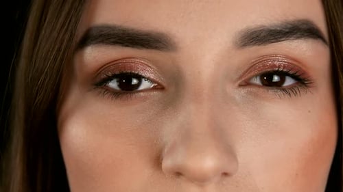 Young Woman's Eyes Close Up on a Black Background. The Girl Opens Her Eyes and Looks at the Camera