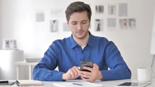 Man Celebrating Success While Using Smartphone in Office