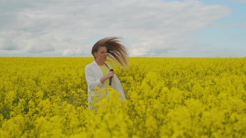 A Mad Woman Singer with a Microphone in a Field of Rapeseed with Yellow Flowers Jumps Shakes Her