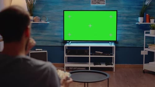 Homme regardant la télévision à écran vert dans le salon