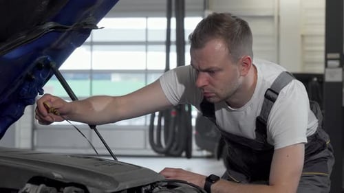 Reifer Automechaniker prüft Öl in einem Auto mit offener Motorhaube