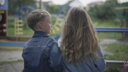 Positiver kaukasischer süßer Schuljunge, der Schulmädchen umarmt, sitzt auf Bank auf Spielplatz