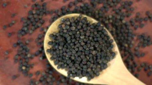 Wooden Spoon with Black Peppercorns on Wooden Surface