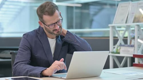 Middle Aged Businessman Having Neck Pain While Using Laptop in Office