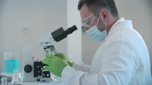 Man in Lab Coat Works With Microscope