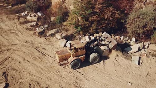 professional bulldozer with a bucket is spreading sand near the stones
