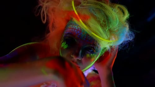 Mysterious Female Character with Fluorescent Makeup on Face Closeup Portrait in Darkness