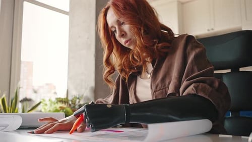 Schöne junge Frau mit Armprothese zeichnet den Plan der Wohnung, während sie am Tisch sitzt