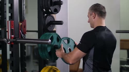 Handsome Strong Man Puts a Disk on the Barbell Turns to the Camera and Smiles Slow Mo