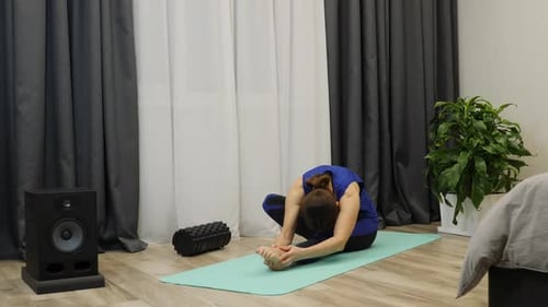 Woman stretches body muscles at home wearing classic blue sportswear. Stretching concept