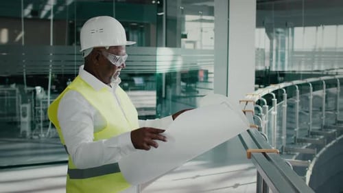 Mature African American Contractor Holding Blueprints Standing In Modern Business Center Building