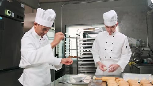 Asian male chefs in uniforms are preparing to bake bread in a stainless kitchen.