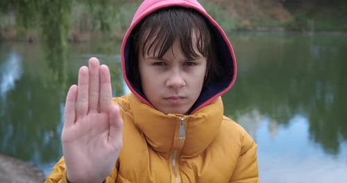Serious Child Gives a Stop Hand Gesture Outdoors