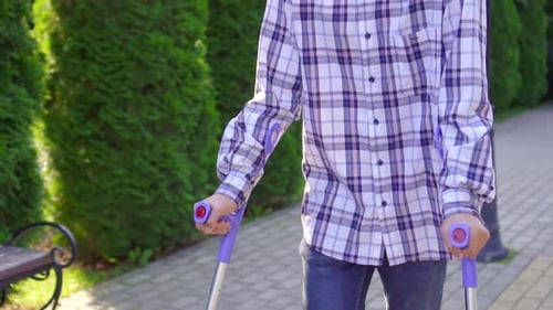 Young Asian Man with Broken Leg on Crutches Walking in Park Slow Mo